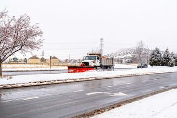Snow plow truck on a wet paved road with snowy sidewalks on a cloudy winter day
