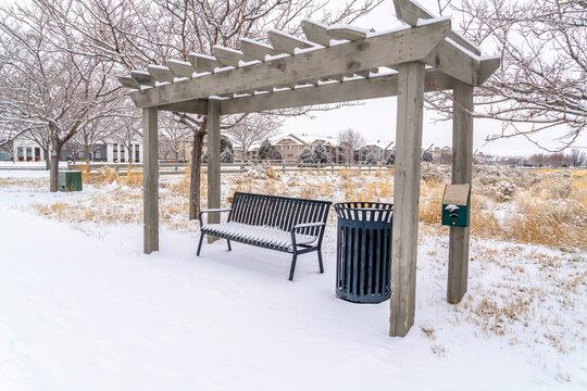 Metal bench and garbage can under wooden pergola on a snowy landscape in winter