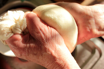 Process of making homemade ricotta cheese. Close-up of female hands with freshly made cottage cheese wrapped in cheese cloth.
