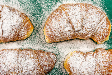 freshly baked croissants with powdered sugar on a green rustic table
