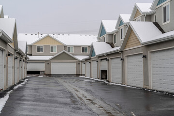 Wet and snowy paved road along white garage doors of apartments in winter view