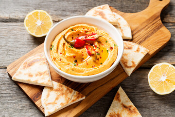 Roasted red pepper hummus with pita bread on wooden background.	