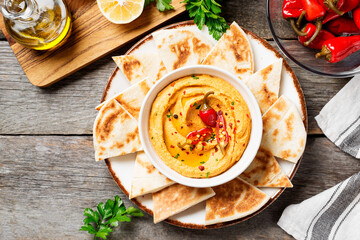 Roasted red pepper hummus with pita bread on wooden background.	top view