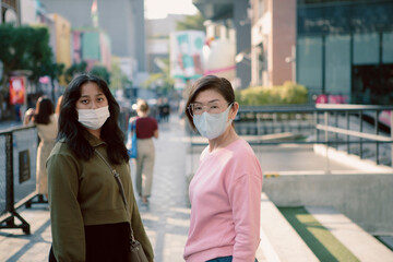 two asian woman wearing protection mask standing on bangkok  city street