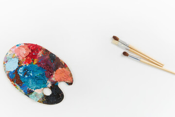 Artist's palette and brushes with different colors isolated on a white background
