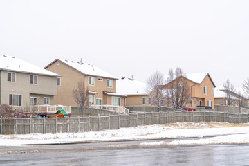 Back view of homes with wooden fences along snowy neighborhood road in winter