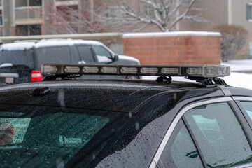 Light bar mounted on the wet roof of a parked black police car on a rainy day