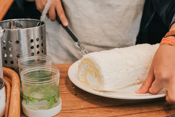 Close up cutting coconut sponge cake roll biscuit or Swiss roll cake (delicious sweet dessert) with knife.