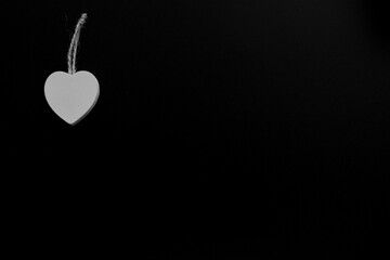 Single white wooden heart isolated on black background. White heart hanging on the jute rope. Texture. Background.