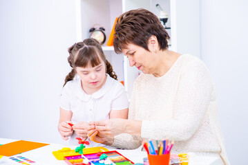 The teacher shows the student with down syndrome how to do creativity. Girl with down syndrome smiles at teacher