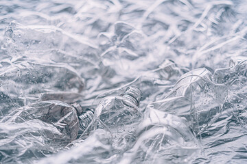 Marine pollution. Waste reduction. Nature conservation. Wet used empty creased plastic bottles pile with water drops on light blur wrinkled texture background.