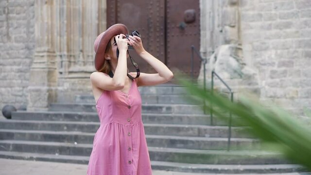 Tourist woman wearing a hat using a vintage film camera to take pictures of Barcelona. Female solo traveler enjoying her vacation in Spain. Photographer working.