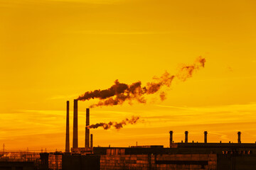 Smoking chimneys against the background of an orange sunset. The concept of the ecological...