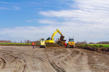 Excavator is loading a truck with ground on building site, road roller compact soil