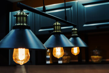 Metal chandeliers in retro style on the background of the kitchen set. Dark room with brightly lit...