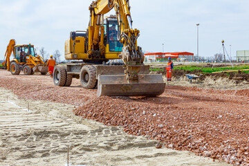 Backhoe is leveling gravel at construction site