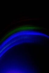 Neon light background. Colorful rays. Defocused blue green red fluorescent glowing rainbow curve lines on dark abstract banner with copy space.