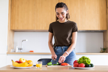 Young pretty woman cutting vegetables in kitchen at home