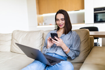 Young woman working with a laptop and mobile phone sitting on a couch at home