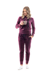 Happy relaxing young woman in home clothes holding coffee or tea mug smiling and looking down. Full body length isolated on white background.