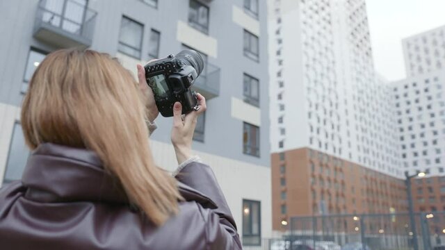 Woman takes photos of buildings with professional camera. Action. Beautiful woman photographer shoots multi-storey buildings. Rear view of female photographer on background of residential buildings