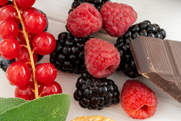 Close up of raspberries with blackberries, chocolate and currants on a white wooden table
