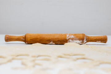 Wooden rolling pin, dough and flour on white table. Cooking process.
