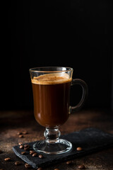Black hot arabica coffee with foam in a glass glass on a dark
