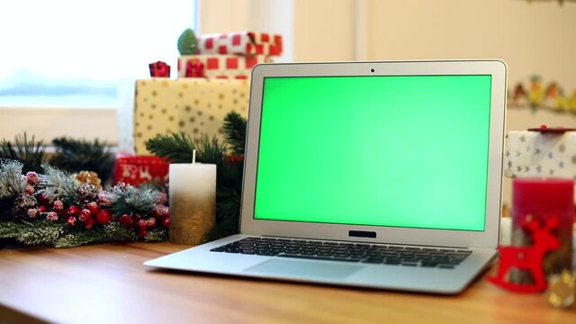 Chroma-key green screen laptop with New Year presents on background. Winter holidays. Connect with friends. Chroma key notebook. Free content. Mockup monitor. Online greeting. Internet surfing. 