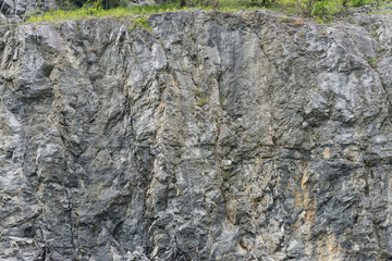 Weathered rock face texture in old stone pit with parts of green. Aged stone wall surface...