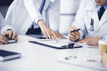 Group of unknown doctors are sitting at the desk and discussing medical treatment, using a clipboard, close-up. Team of physicians at work in a clinic. Medicine and healthcare concept - 402809099