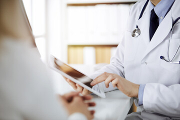 Unknown male doctor and patient woman discussing current health examination while sitting in sunny...
