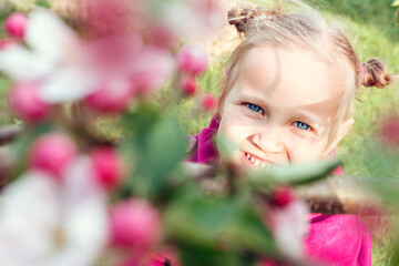 Naklejka premium Little girl in the spring garden near the flowers. A child in a purple coat in the garden