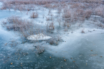 Frozen lake at wintertime at an abandoned water dam, lifeless vegetation.