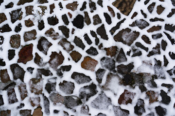 A path of different natural stones is partially covered with snow, winter texture for wallpaper and...
