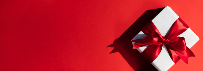 Holiday present. Women Day. White gift box with ribbon bow isolated on red festive copy space background. Special occasion congratulation. Greeting card.