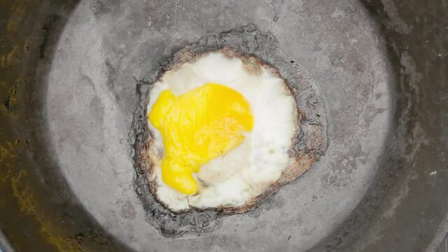 An egg in a pan, cooking for too long and becoming dark at the borders. Overhead closeup shot.
