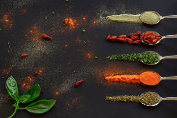 Cucharas con especias, pimienta, gindillas, oreganosobre mesa color oscuro