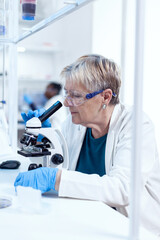 Concentrated senior scientist conducting genetic experiment using microscope. Elderly researcher...