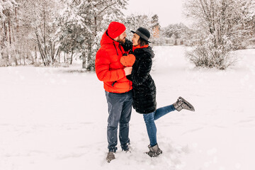 Fototapeta na wymiar Young romantic couple is having fun outdoors in winter. Snowing. Love and leisure concept. Enjoying spending time together. Heart with sequins. Two lovers are hugging and kissing in Saint Valentine's 