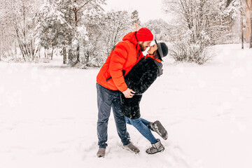 Fototapeta na wymiar Young romantic couple is having fun outdoors in winter. Snowing. Love and leisure concept. Enjoying spending time together. Two lovers are hugging and kissing in Saint Valentine's 
