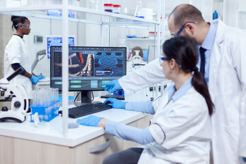 Group of scientist working with computer in laboratory. Team of researchers doing pharmacology engineering in sterile lab for healthcare industry with african assistant in the background.