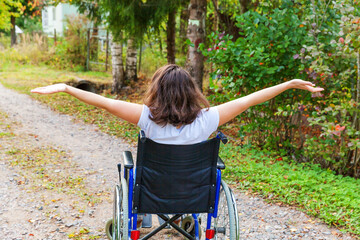 Young happy handicap woman in wheelchair on road in hospital park enjoying freedom. Paralyzed girl...