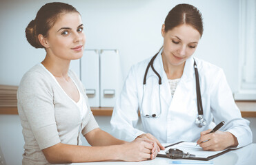 Doctor and patient are sitting and discussing health examination results in clinic office. Health care, medicine and good news concepts