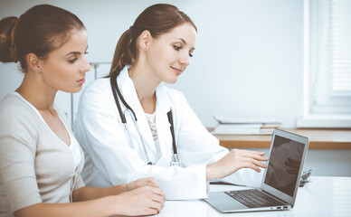 Fototapeta premium Doctor and patient are sitting and discussing health examination results while using laptop computer. Health care, medicine and good news concepts