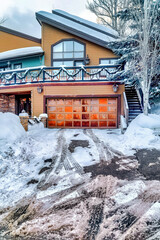 Tire tracks on snowy driveway leading to panelled metal garage door of home