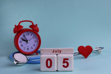 July 5. White wooden calendar blocks with date, clock and stethoscope on blue pastel background. Selective focus. health concept