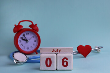 July 6. White wooden calendar blocks with date, clock and stethoscope on blue pastel background....