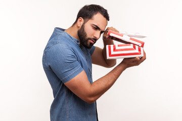 Side view nosy curious man with beard taking a look inside gift box, unpacking present to know what...