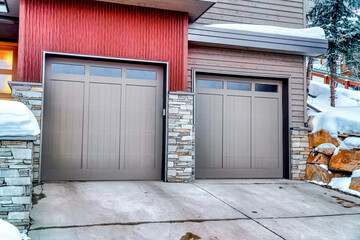 Home facade with glass panelled gray garage doors against snowy slope in winter
